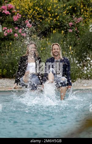 Coppia seduta al bordo della piscina e spruzzi d'acqua Foto Stock