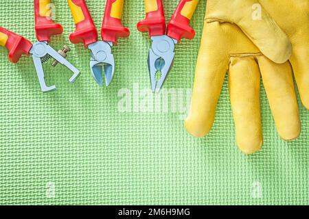 Set di guanti di protezione in pelle spelafili isolanti pinze su concetto di elettricità di superficie verde. Foto Stock