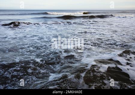 Onde schiumose che si rompono sulla riva Foto Stock