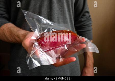 Un uomo tiene un pesce rosso impaccato sotto vuoto. Bellissimo tonno Foto Stock