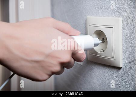 Primo piano della mano di una donna che inserisce un caricabatterie usb bianco in una presa da 220 volt Foto Stock