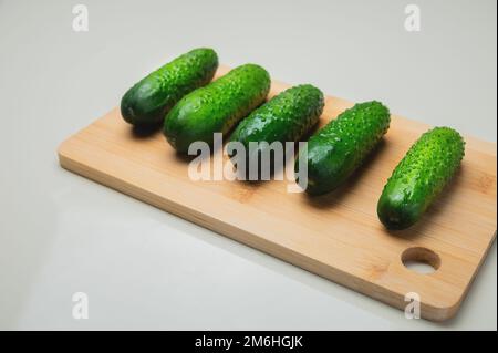 Primo piano di diversi cetrioli freschi si trovano su un tagliere di legno su un tavolo bianco. copia spazio cibo vegetariano Foto Stock