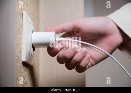 Primo piano della mano di una donna che inserisce un caricabatterie usb bianco in una presa da 220 volt Foto Stock