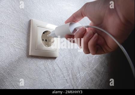 Primo piano della mano di una donna che inserisce un caricabatterie usb bianco in una presa da 220 volt Foto Stock