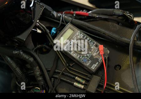 Un meccanico che utilizza un multimetro controlla il livello di tensione della batteria di una motocicletta in un'officina. Primo piano Foto Stock