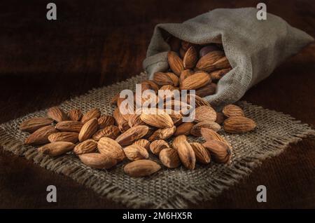 Mandorle in un sacchetto tessuto su uno sfondo di legno scuro Foto Stock