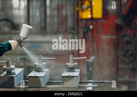 Rivestimento con primer per polveri di parti metalliche. L'uomo di lavoro in un vestito protettivo spruzza la vernice della polvere dalla pistola sulla costruzione del prodotto di metallo Foto Stock