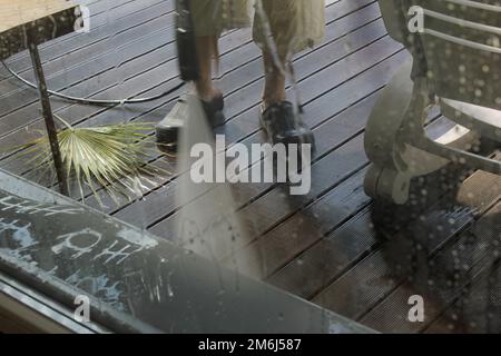 Lavaggio superficie di potenza. Uomo che pulisce la terrazza con una lavatrice elettrica. Pulitore ad alta pressione su superfici di terrazze in legno e mobili da esterno. Foto Stock