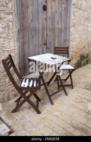 Sedie di legno coperte di neve vuote e tavolino da caffè su un sentiero in pietra. Foto Stock