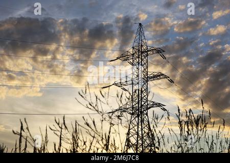 Silhouette di torre ad alta tensione con fili elettrici e erba secca sullo sfondo del cielo e delle nuvole del tramonto. Linee di trasmissione dell'elettricità Foto Stock