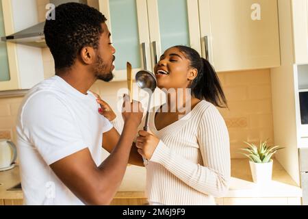 coppia ispanica cantando insieme tenendo un mestolo come un microfono in cucina Foto Stock