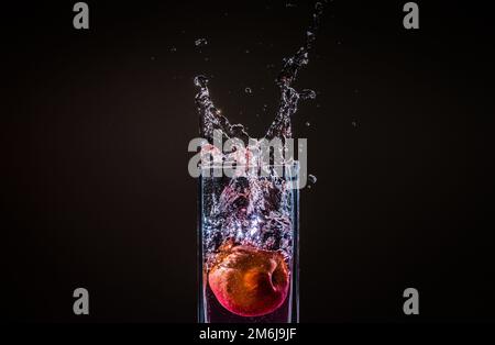 L'acqua che fuoriesce da un bicchiere con una mela in esso isolato su uno sfondo nero Foto Stock