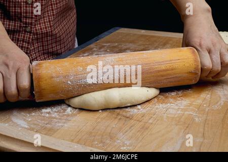 Una foto ravvicinata di come stendere l'impasto fresco su un tagliere di legno. Foto Stock