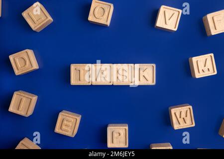 COMPITI la parola su cubetti di legno con mano di legno su sfondo blu . Concetto di business e finanza Foto Stock