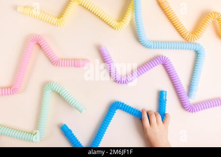 Giocattoli alla moda per bambini color pastello pop-tube nelle mani del bambino su sfondo beige. Set di forme e colori tubo corrugato e. Foto Stock