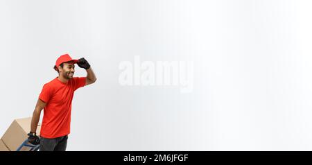 Concetto di consegna - Ritratto del Bell'uomo di consegna Africano Americano o corriere che spinge il camion della mano con la pila delle scatole. Isolare Foto Stock