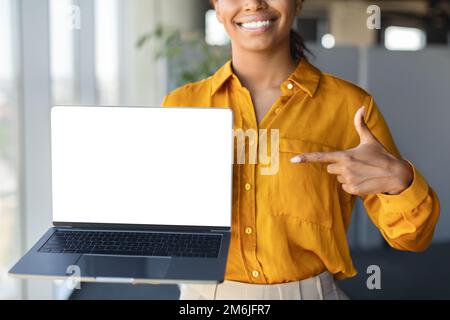 Imprenditore nero femmina che punta al computer portatile con schermo vuoto per il disegno di Web site, in piedi in ufficio, mockup Foto Stock