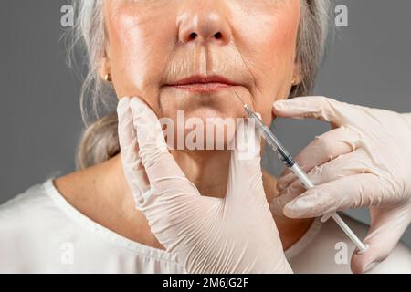 Donna europea matura seria su procedura, cosmetologa mani in guanti fare l'iniezione botox Foto Stock