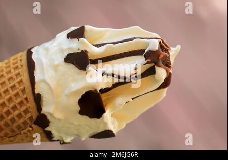 Primo piano di un delizioso cono gelato con waffle, gelato alla vaniglia e glassa al cioccolato. Foto Stock