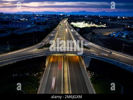 Vista aerea del drone dello svincolo autostradale. Le macchine rotatorie si muovono velocemente. Infrastrutture di trasporto Foto Stock