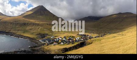 Villaggio di Gjógv sotto la montagna di Middagsfjall e la montagna di Slættaratindur coperta da nuvole Foto Stock