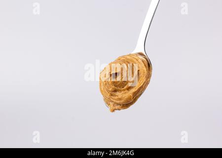 Il delizioso burro cremoso di arachidi è disposto in un bellissimo vetrino in un cucchiaio su uno sfondo bianco. Colazione gustosa. Concetto di cibo sano Foto Stock