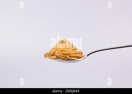 Il delizioso burro cremoso di arachidi è disposto in un bellissimo vetrino in un cucchiaio su uno sfondo bianco. Colazione gustosa. Concetto di cibo sano Foto Stock