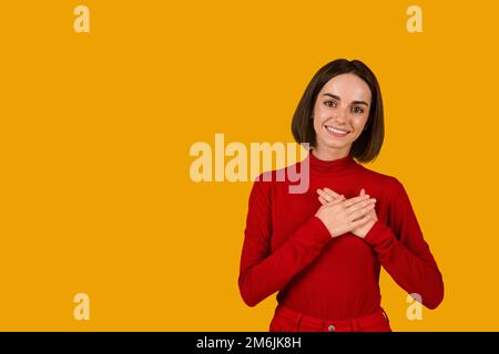 Giovane donna grata che tiene le mani sul petto Foto Stock