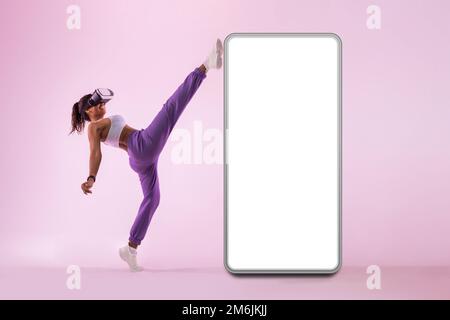 Ragazza sportiva in realtà virtuale googles esplorare gioco di fitness realtà virtuale vicino enorme smartphone con spazio libero, mockup Foto Stock
