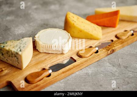Assortimento di vari tipi di formaggi serviti sulla tavola di legno con forcella e i coltelli Foto Stock