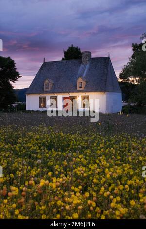 Vecchia casa in stile cottage del regime francese del 1752 illuminata al tramonto in estate, Saint-Francois, Ile d'Orleans, Quebec, Canada. Foto Stock