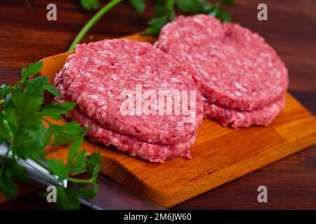 Cotolette di carne cruda con prezzemolo su tavola di legno Foto Stock