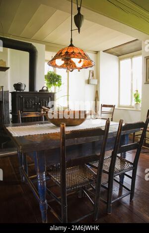 Tavolo da pranzo e sedie in legno dipinto di blu antico con forno a legna in ghisa nera nella cucina originale e sala da pranzo all'interno di una vecchia casa del 1785. Foto Stock