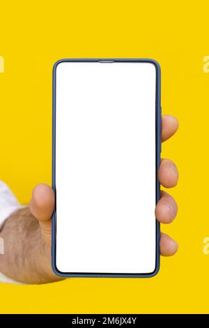 Primo piano uomo che tiene lo smartphone con schermo bianco vuoto e custodia blu del telefono. Isolato su sfondo giallo. Telefono cellulare fr Foto Stock