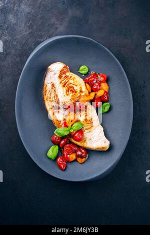 Bistecca di pesce spada fritto con pomodori e paprika servita come vista dall'alto su un piatto di design Foto Stock