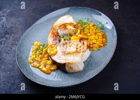 Bistecca di pesce spada fritto con chutney di mango ed erbe servite come primo piano su un piatto di design Foto Stock