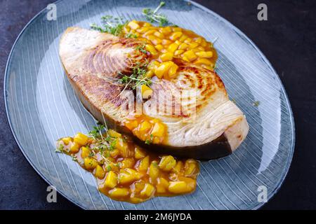 Bistecca di pesce spada fritto con chutney di mango ed erbe servite come primo piano su un piatto di design Foto Stock