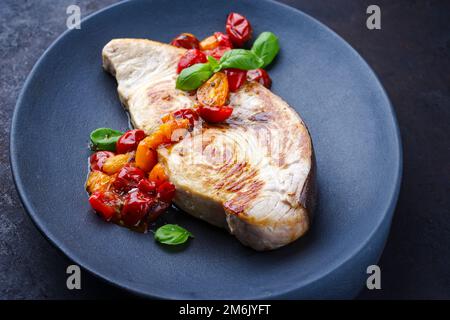 Bistecca di pesce spada fritto con pomodori e paprika servita da primo piano su un piatto di design Foto Stock