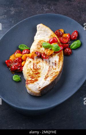 Bistecca di pesce spada fritto con pomodori e paprika servita da primo piano su un piatto di design Foto Stock