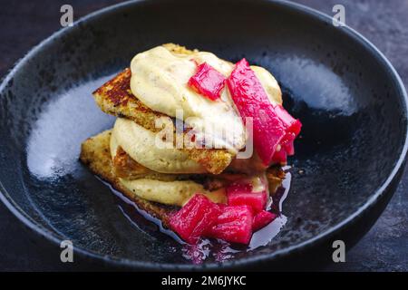 Tiramisù panettone tradizionale italiano arrosto con crema alla vaniglia cagliata e rabarbaro servito come primo piano in una ciotola dal design nordico Foto Stock