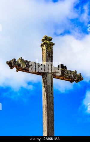 Antico crocifisso cattolico in pietra coperto da piante parassitarie e muschio Foto Stock