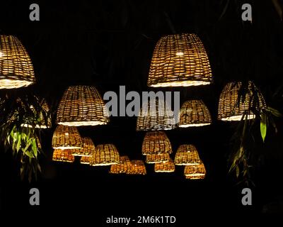 Molte lampade con paralumi in vimini sono appese in un parco di bambù scuro. Foto Stock