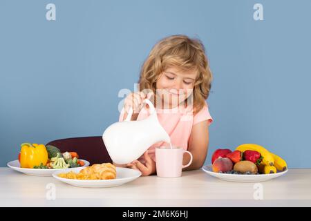 Capretto con latte di latte. Capretto che versa latte intero di mucche. Ritratto di bambino mangiare cibo fresco sano in cucina a casa. Il ragazzo che mangiava prima la colazione Foto Stock