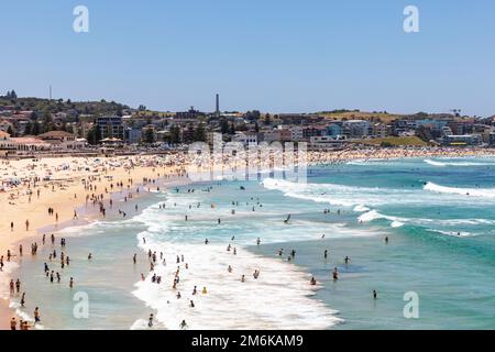 2023 Bondi Beach in una giornata estiva con cielo sereno, la spiaggia è affollata di persone che prendono il sole e altri che si rilassano nuotando nell'oceano, Sydney, NSW, Australia Foto Stock