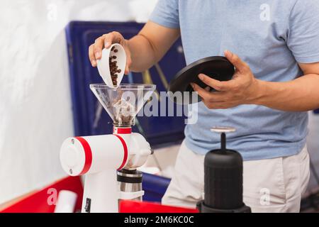 Barista che versa i chicchi di caffè nel macinacaffè per preparare il caffè nero. Foto Stock