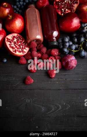 Vari frutti di colore rosso, viola e nero. Mix di frutta e succhi di frutta in bottiglia su nero Foto Stock