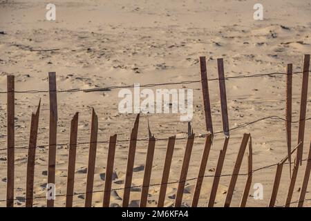 Una recinzione in una duna di sabbia con molte linee diagonali e luce del sole che getta ombre. Foto Stock