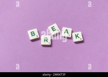 Rottura formata da piastrelle scrabble su sfondo lilla. Foto Stock