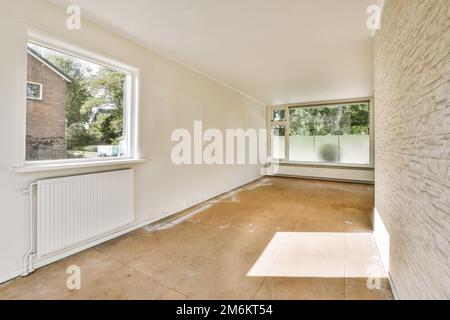 an empty room with wood flooring and white paint on the walls there is a large window in the corner Stock Photo