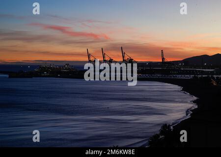 Vista tramonto con silhouette di gru industriali nel porto di Malaga, Andalusia, Spagna. Foto Stock